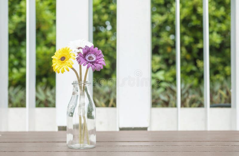 Цветок крупного плана искусственный красочный на прозрачной стеклянной бутылке на деревянном стуле в предпосылке вида на сад
